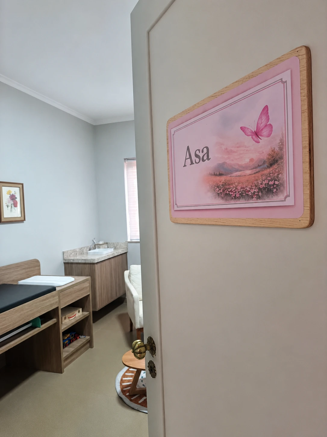 Porta da sala Asa, com plaquinha de borboleta e maca infantil ao fundo