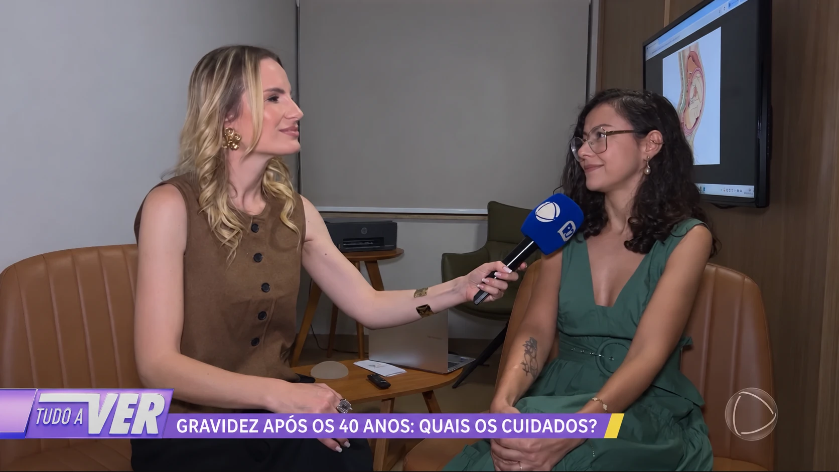 Dra. Priscila Lugarinho sendo entrevistada para o programa Tudo a Ver sobre gravidez após os 40 anos, ao lado da tela com a ilustração de um bebê no útero