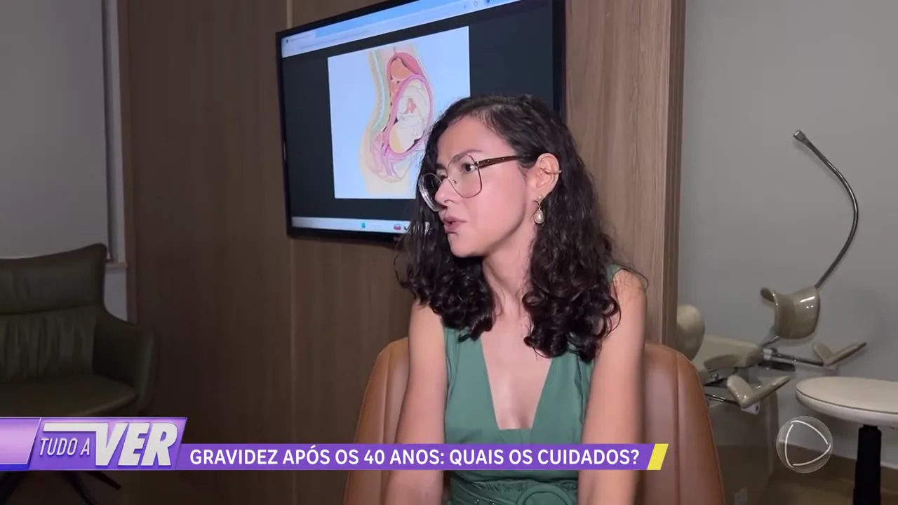 Dra. Priscila Lugarinho durante a entrevista no consultório, ao lado da tela com a ilustração de um bebê no útero